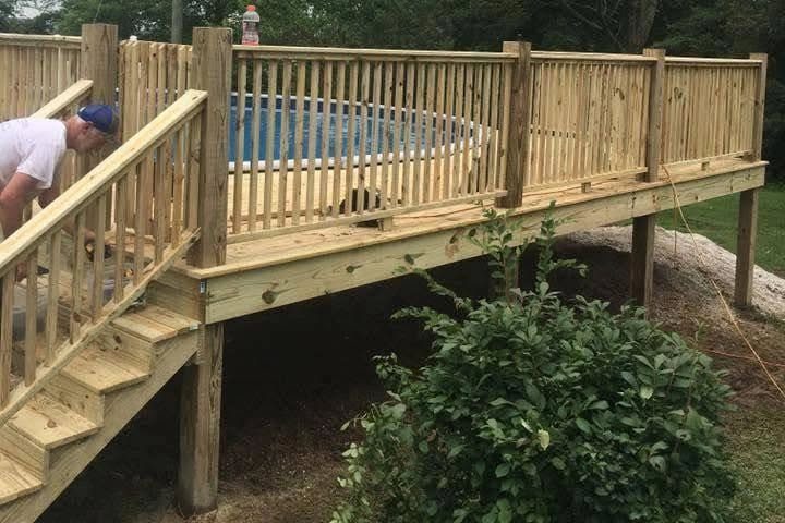 Crew member finishing a pressure-treated wood deck with railings built around an above-ground pool