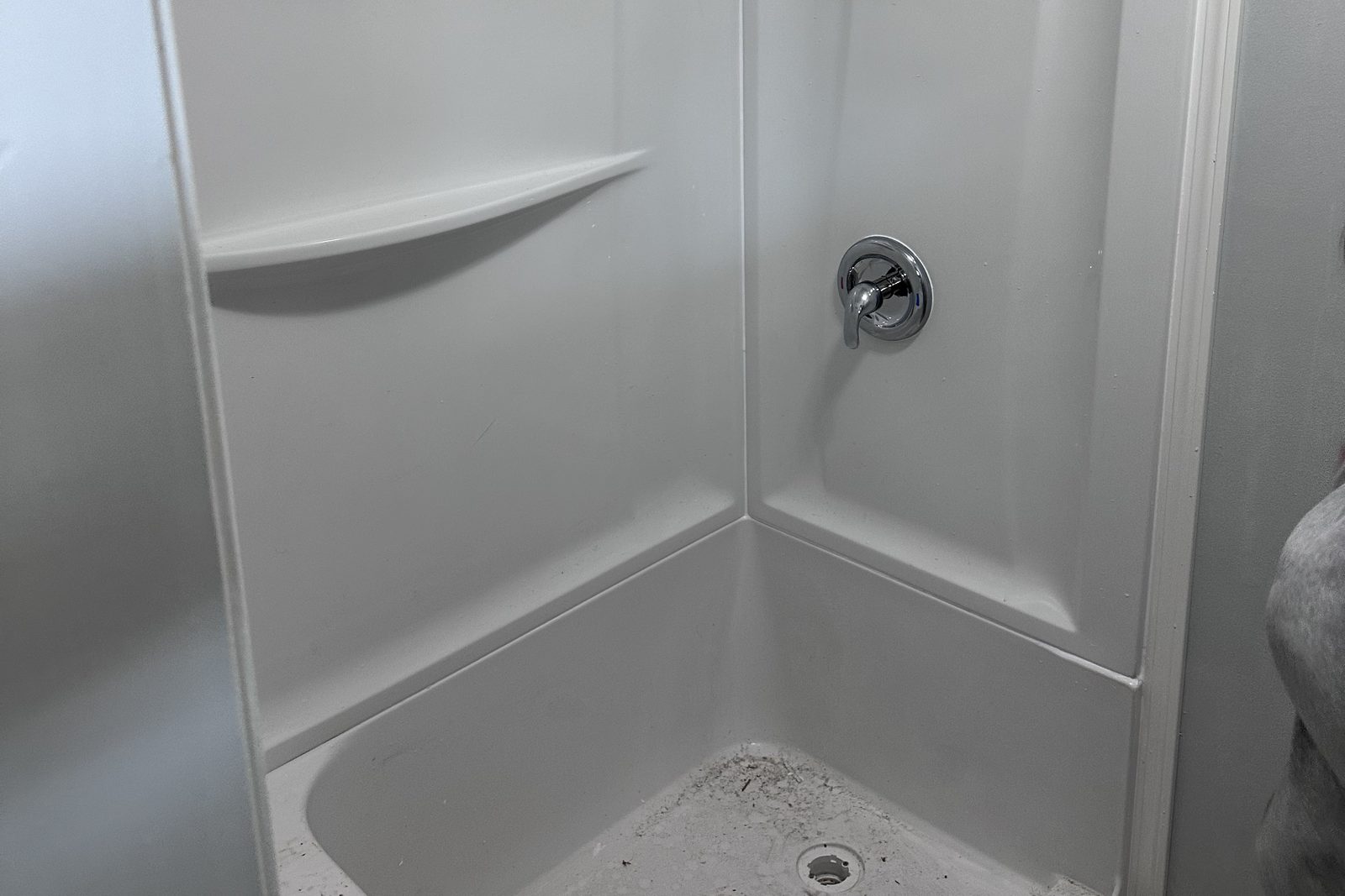 Newly installed white corner shower surround with built-in shelves and a molded seat in Clarkson, KY