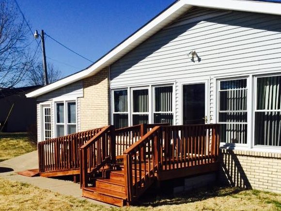 Stained wood deck with railings and two sets of steps on a white-sided brick home in Clarkson, KY