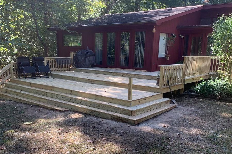 New ground-level pressure-treated deck with wide steps beside a red-sided house in the woods at Nolin Lake, Kentucky