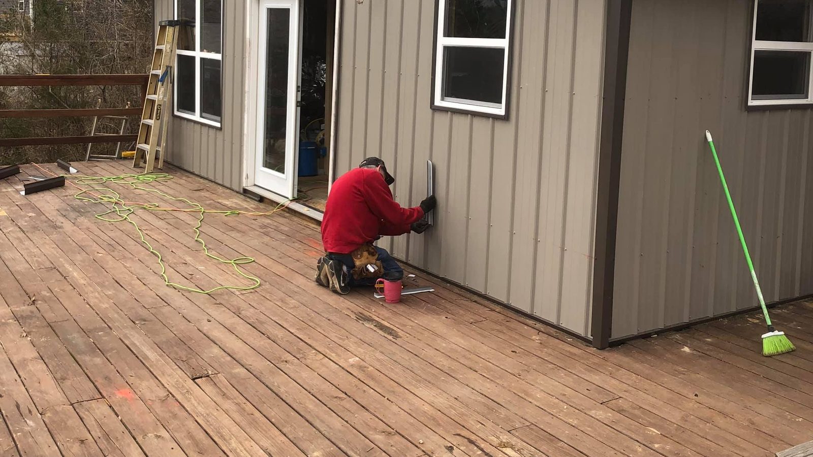 Crew member fastening board-and-batten siding on a small building set on a large wood deck — Clarkson, KY