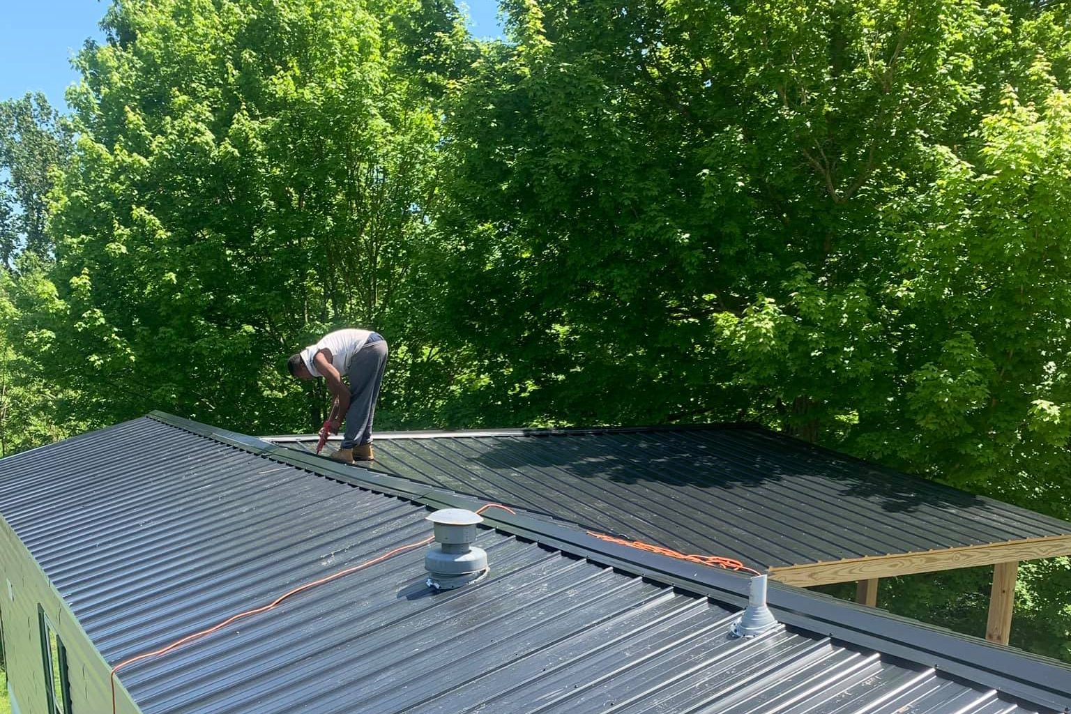 Roofer fastening new dark gray metal roofing panels around a vent boot — Grayson County, Kentucky
