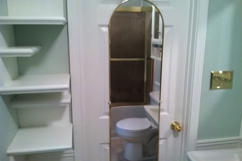 Remodeled bathroom with built-in white shelves and an arched mirror on the door — Kentucky
