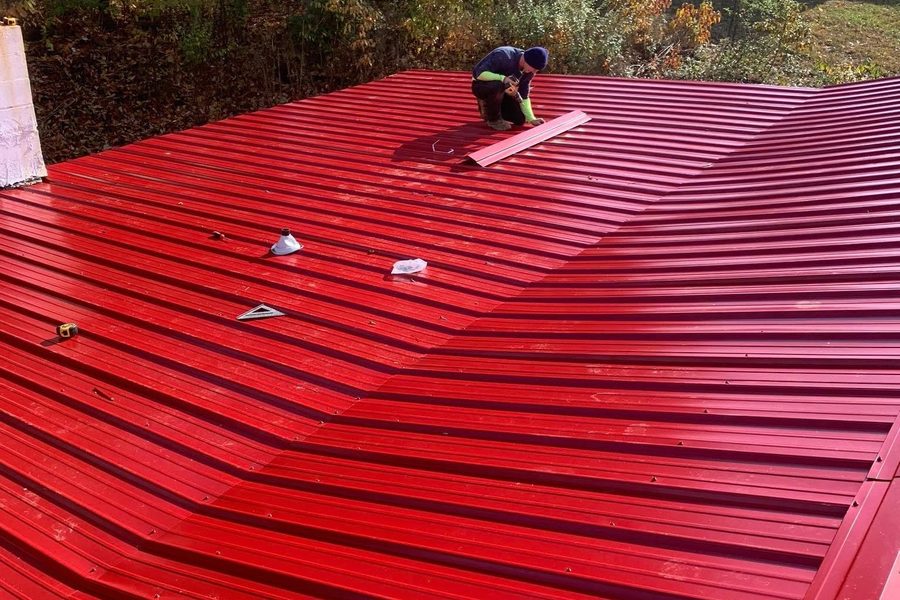 Crew member fastening new red metal roofing panels on a house