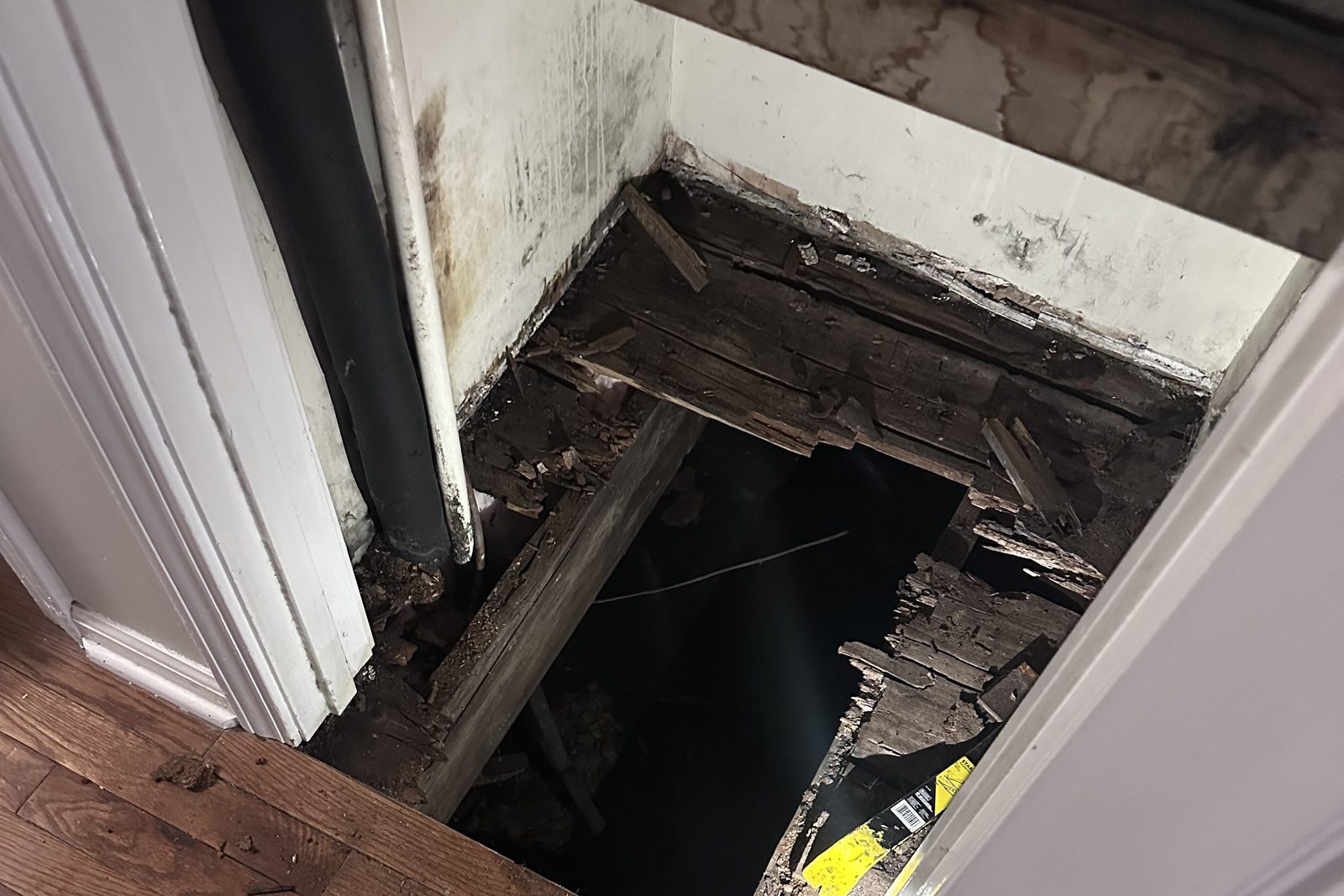 Floor opened up at a doorway, showing rotted subfloor and joists down to the crawlspace