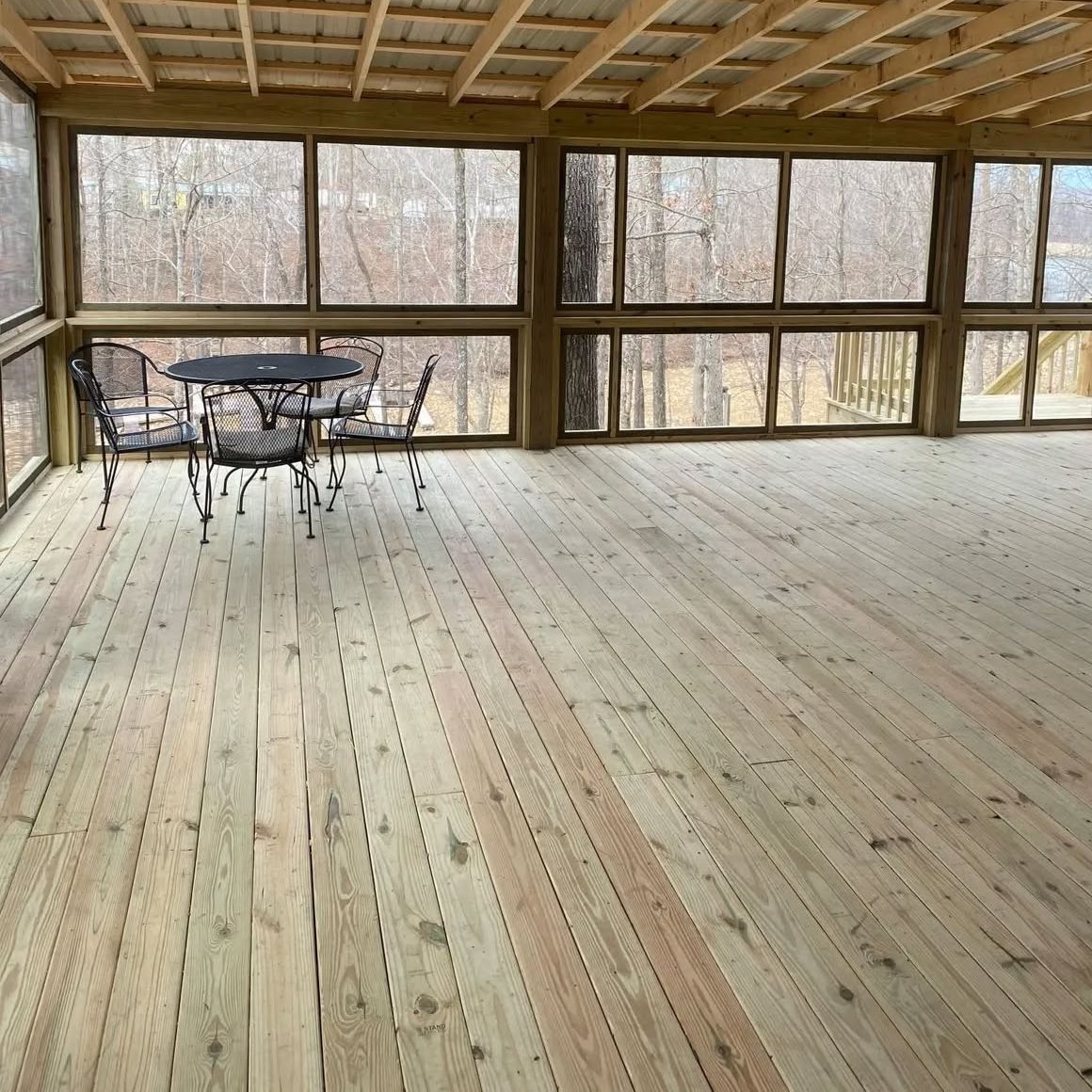 Screened-in porch with pressure-treated floor, exposed rafters and a patio table set